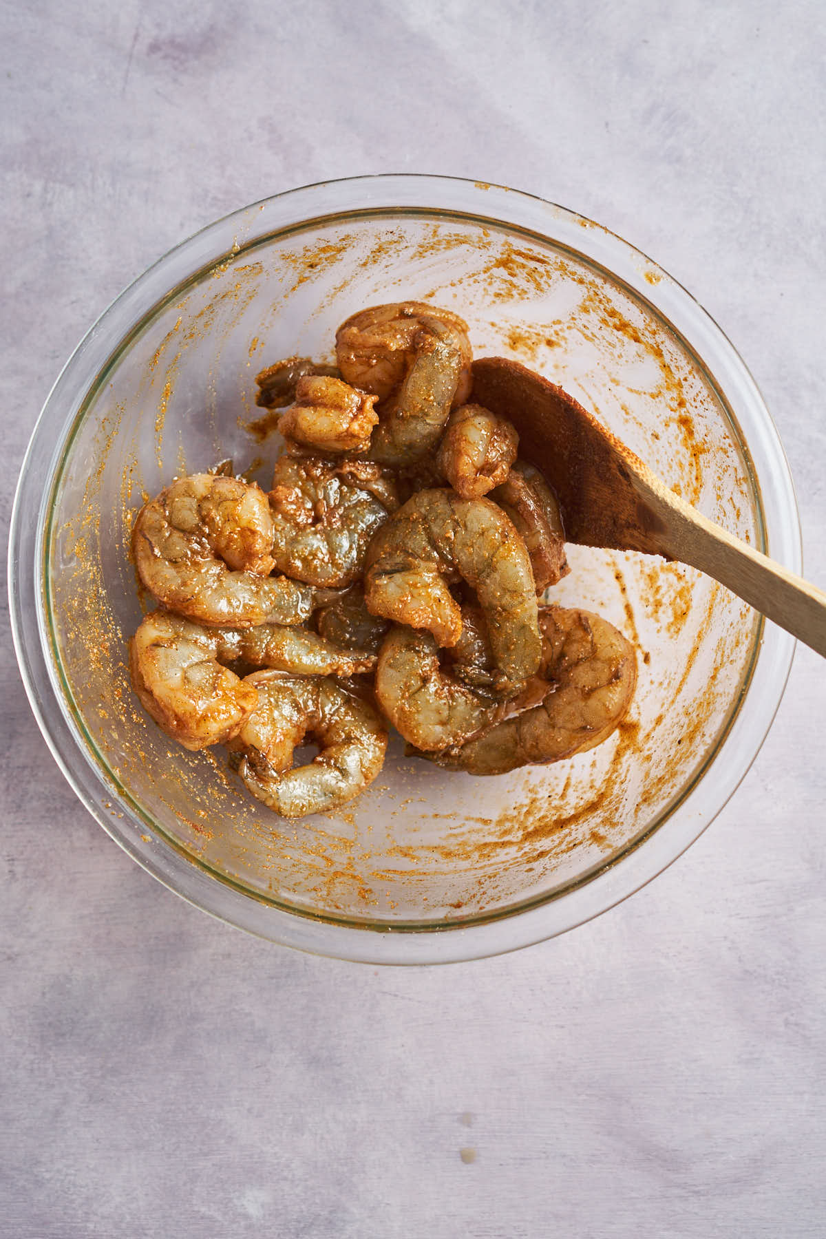 Shrimp tossed with Cajun seasoning in a glass bowl with a wooden spoon.