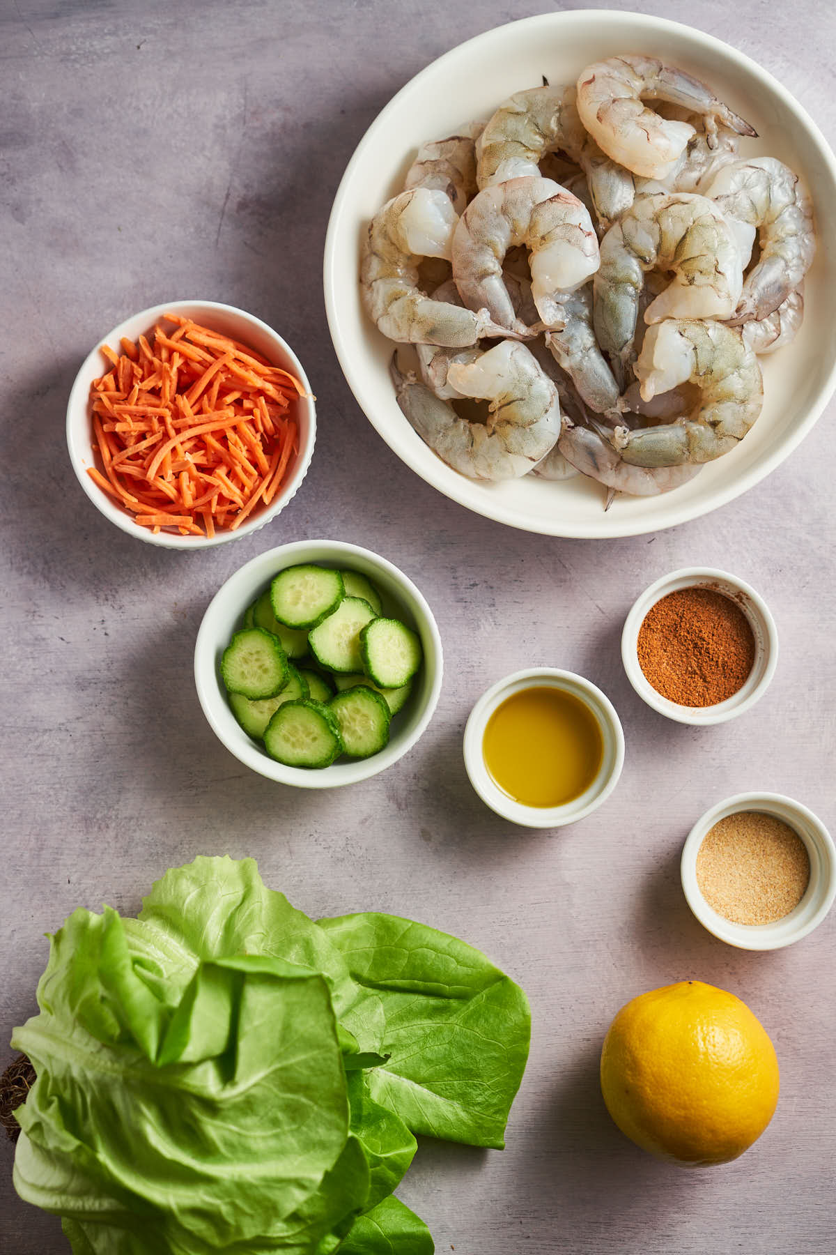 Raw shrimp, lettuce, shredded carrots, cucumber, Cajun seasoning, oil, garlic powder, and lemon for Cajun shrimp lettuce wraps.