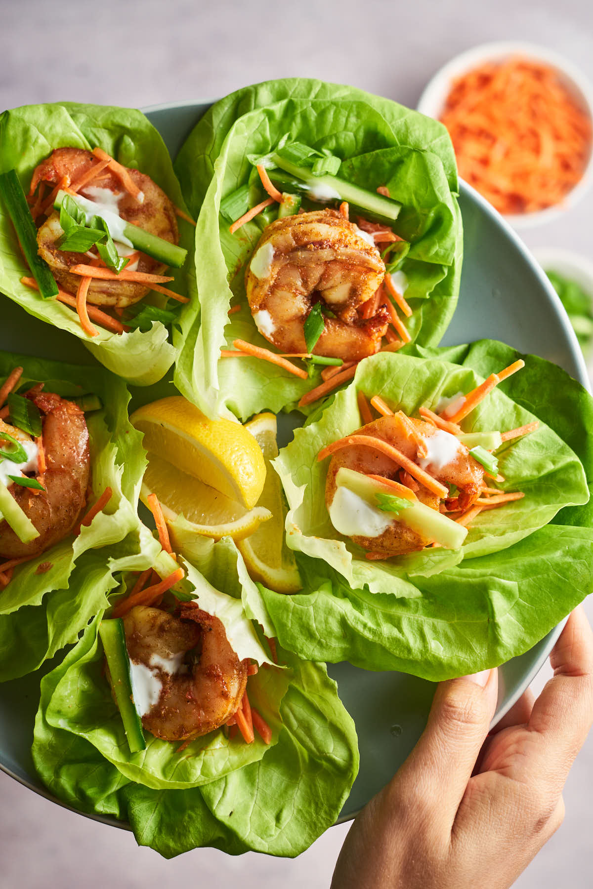A hand holding a plate of Cajun shrimp lettuce wraps with vegetables and a creamy drizzle.