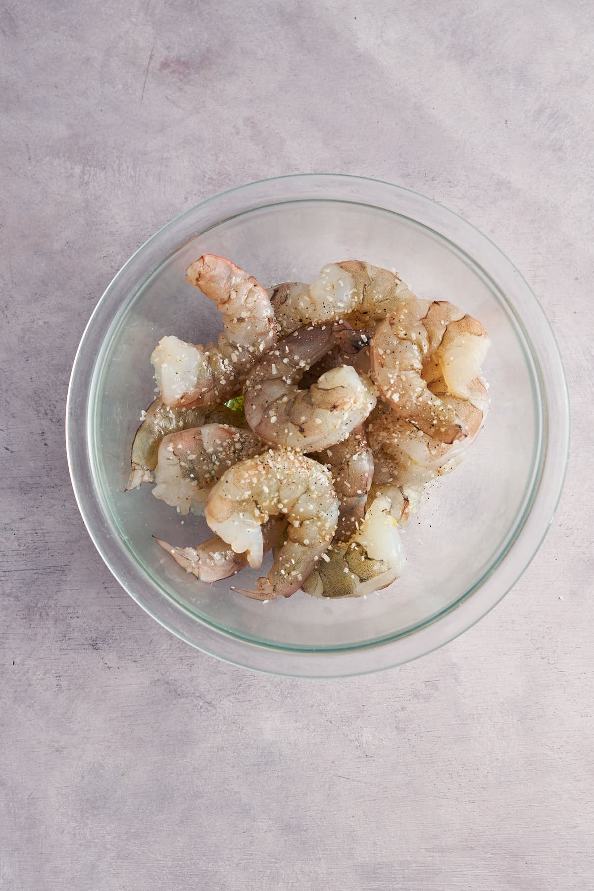 Raw peeled shrimp in a glass mixing bowl.