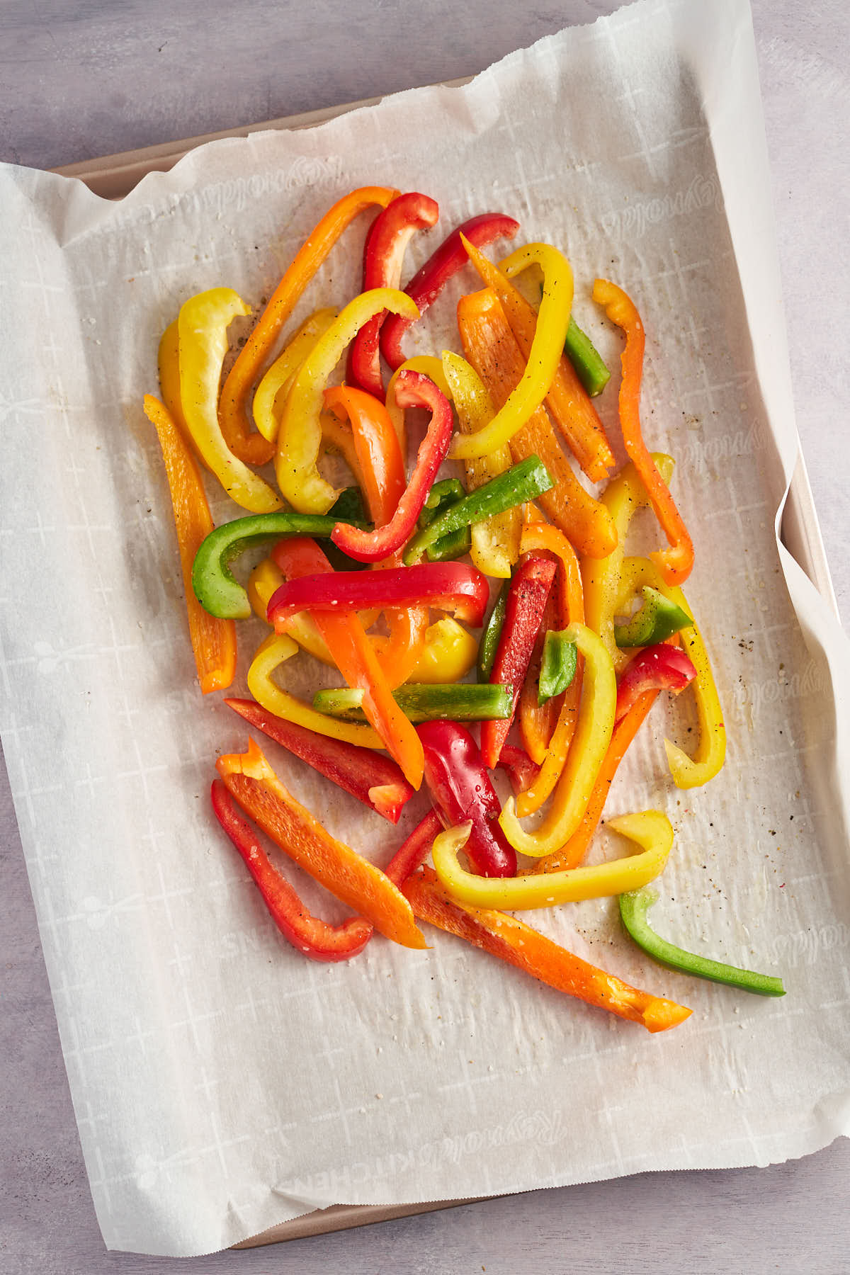 Sliced colorful bell peppers spread on a parchment lined sheet pan