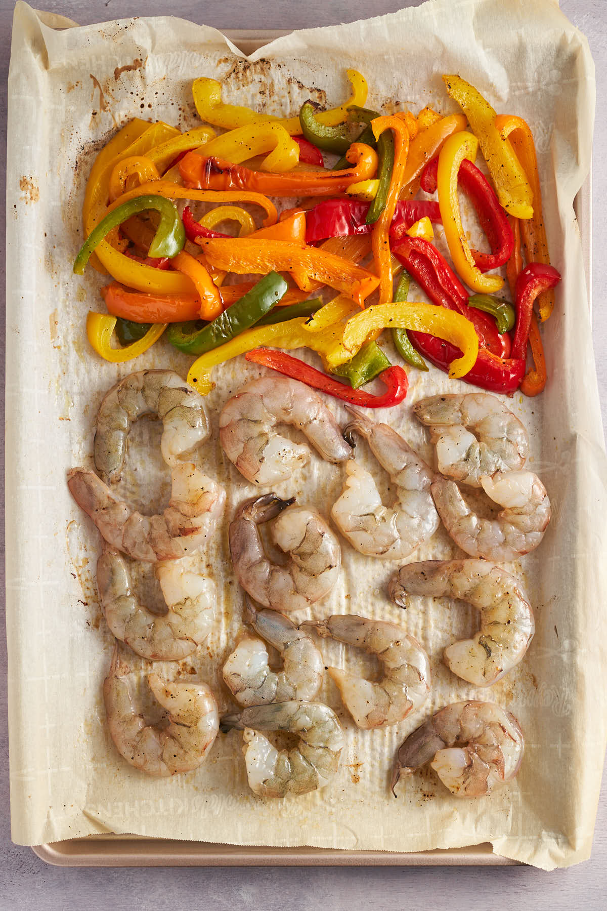 Raw shrimp arranged beside bell peppers on a parchment lined sheet pan.