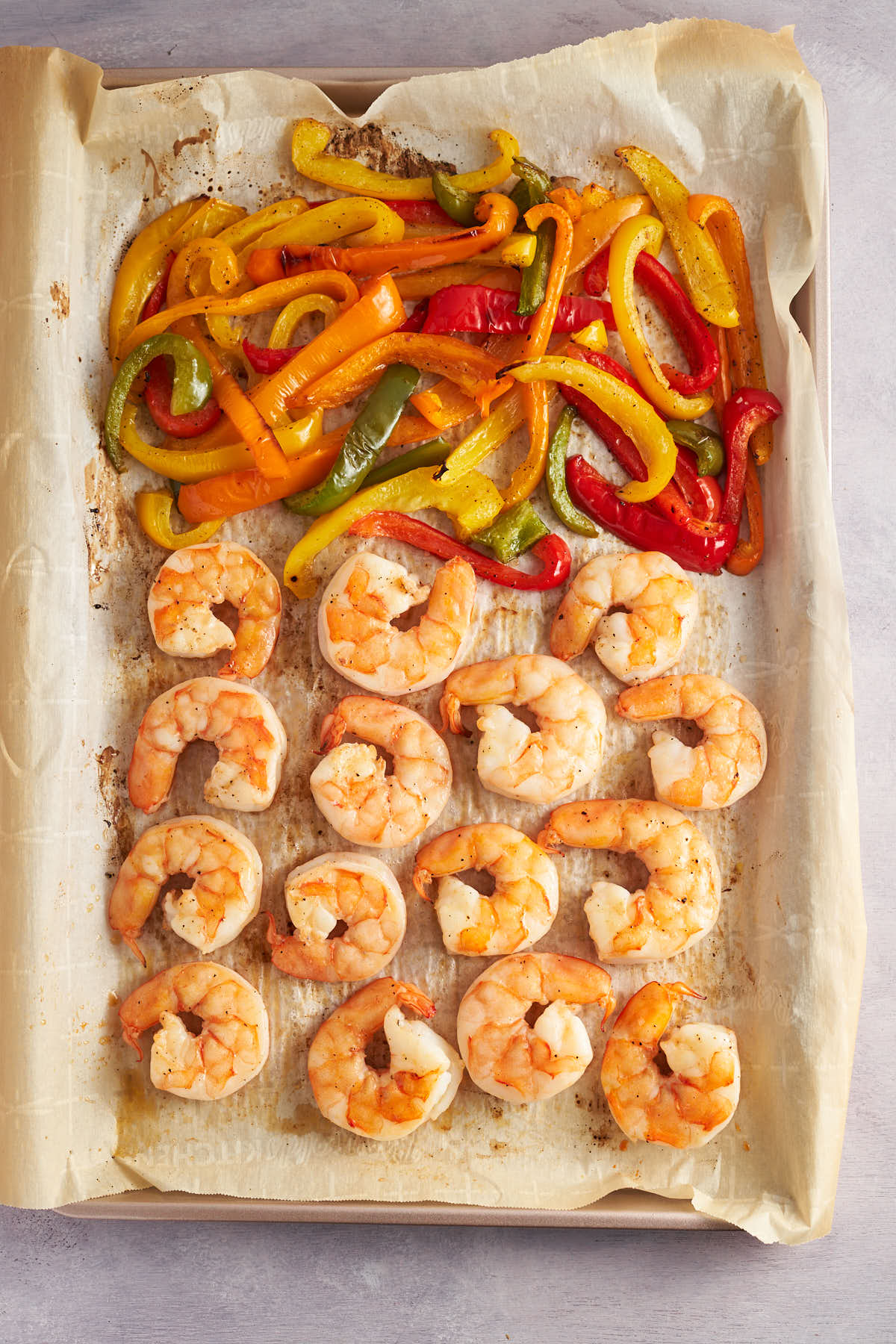 Cooked shrimp and roasted bell peppers on a parchment lined sheet pan.