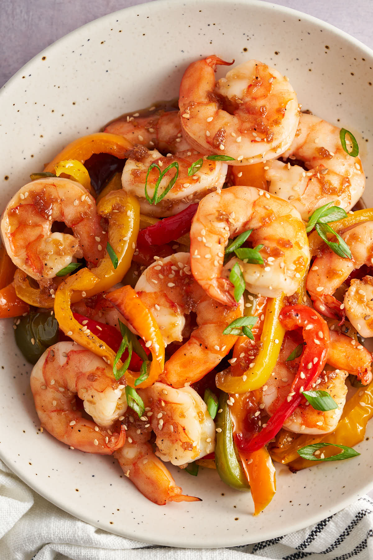 Close-up of honey garlic shrimp and bell peppers topped with sesame seeds and green onions.