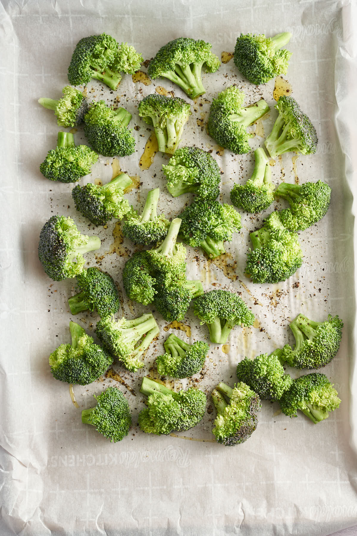 Broccoli florets coated with oil and seasonings on a sheet pan.
