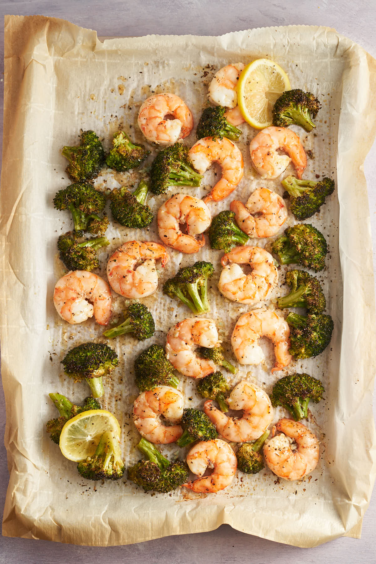 Baked lemon garlic shrimp with roasted broccoli and lemon slices on a parchment lined sheet pan.