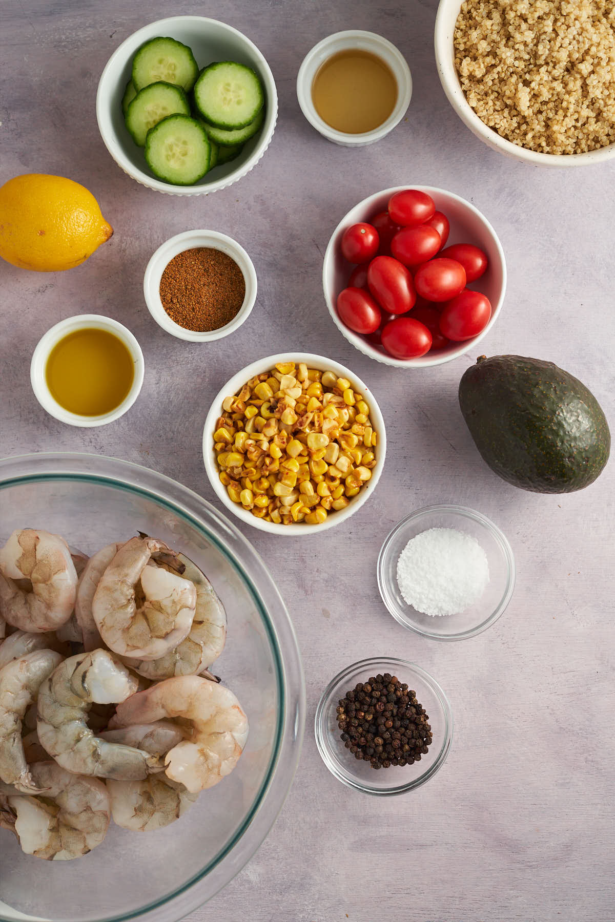 Ingredients for Old Bay shrimp bowls, including shrimp, quinoa, corn, cucumber, cherry tomatoes, avocado, lemon, oil, and seasoning