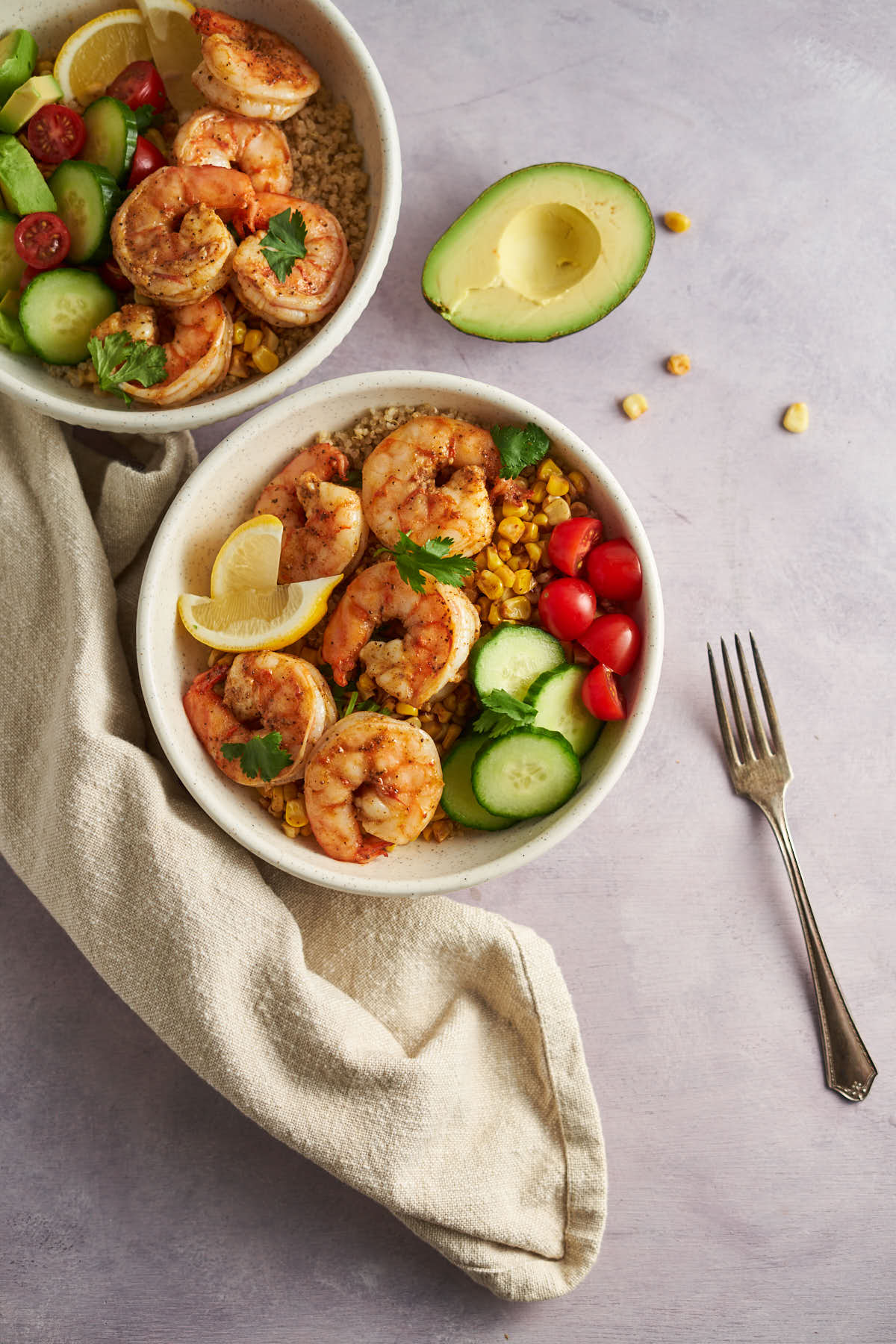 Overhead view of two Old Bay shrimp bowls with quinoa, corn, cucumber, tomatoes, and lemon