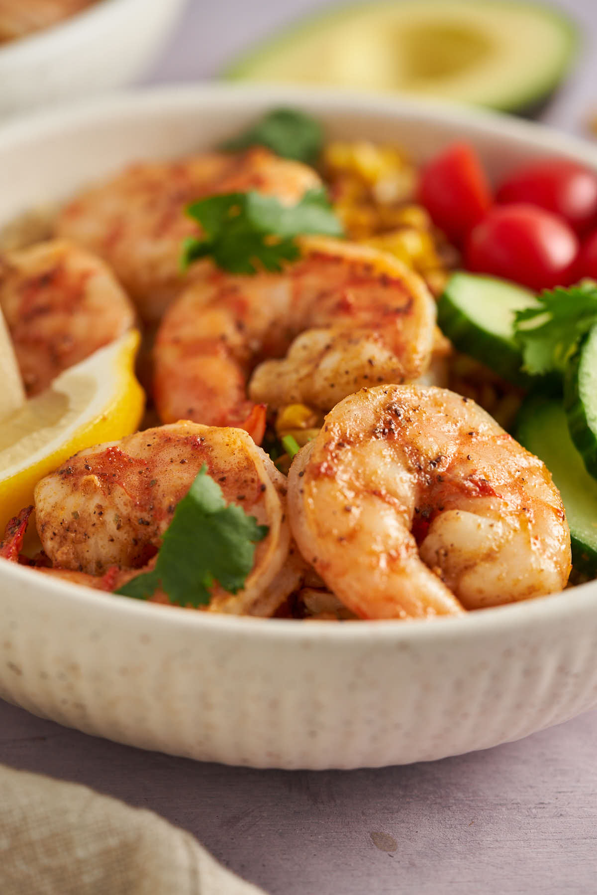 Old Bay shrimp topped with cilantro in a quinoa bowl with corn, cucumber, tomatoes, and lemon